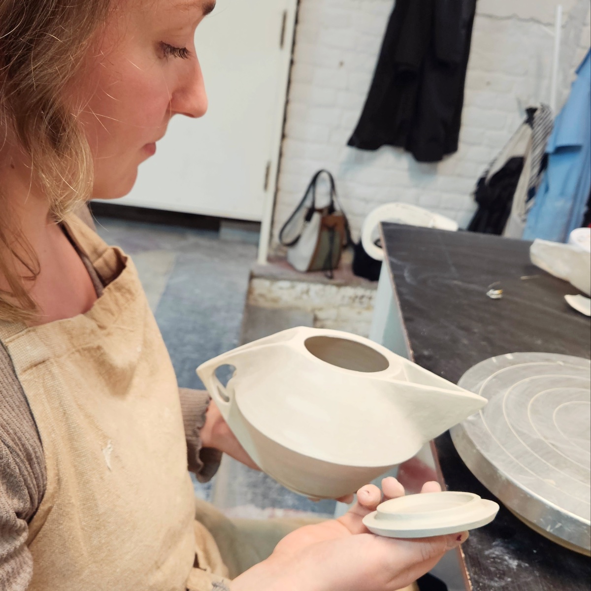 Clémence tient une théière crue et son couvercle dans l'atelier