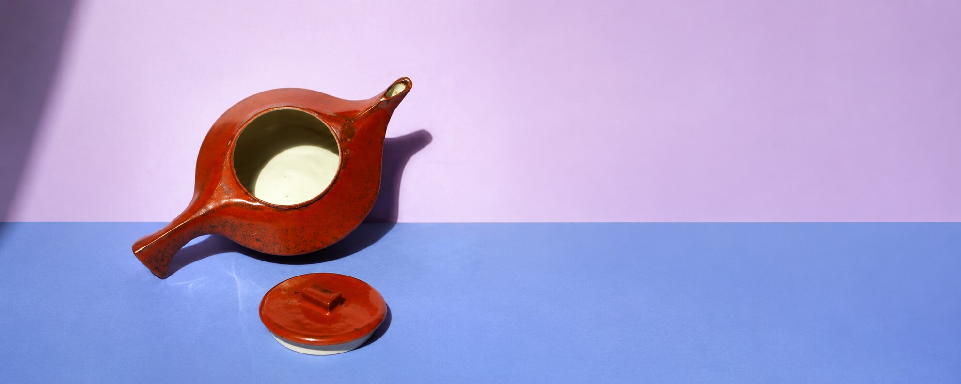 Théière Petite Lampe en grès, émail brique brillant, ouverte, avec son couvercle posé devant, sur un papier de fond lavande et pervenche
