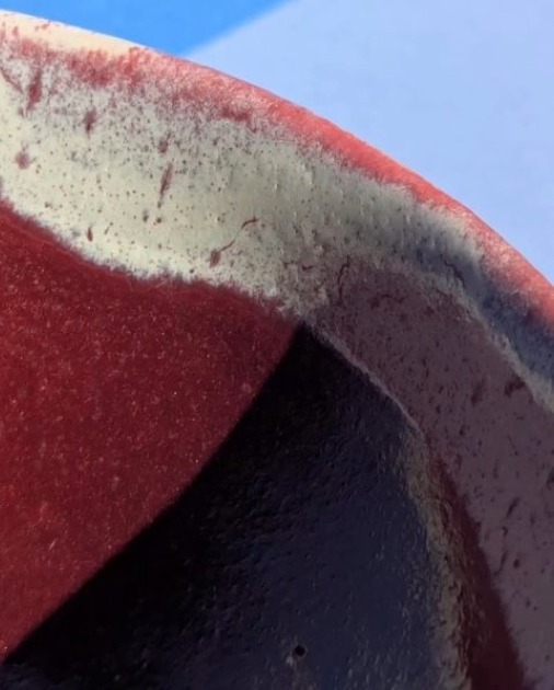 Gros plan sur un bord de pièce émaillé : rouge, crème et bleu nuit