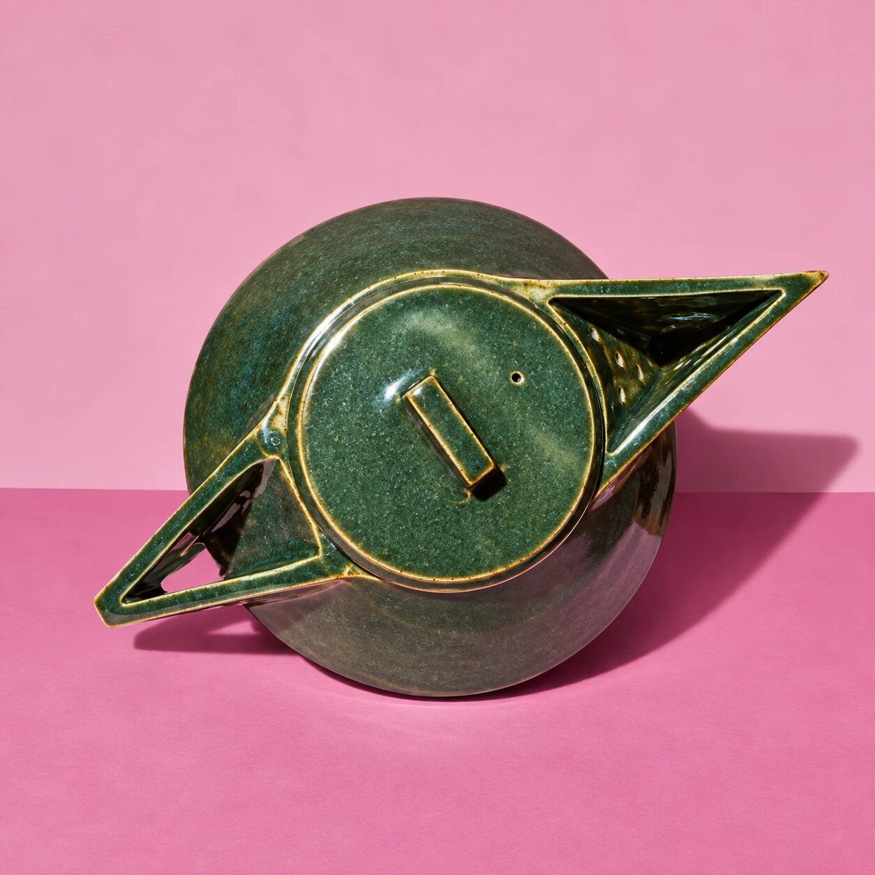 Pièce « Soucoupe Volante » : émail vert profond, deux ailes triangulaires, sur un papier de fond rose